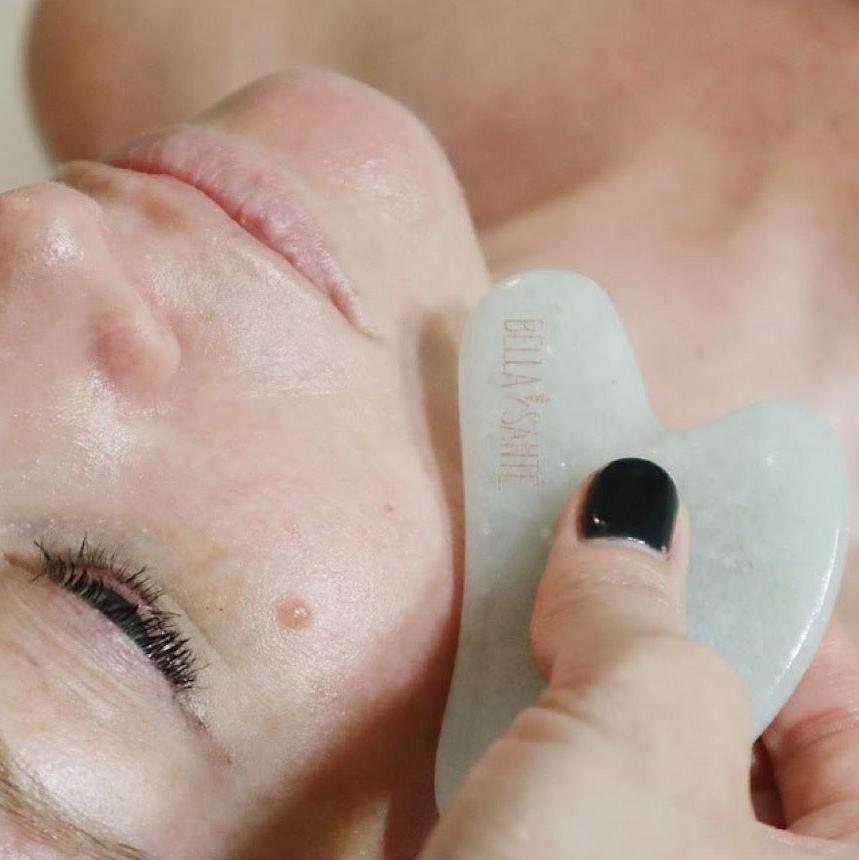 Woman receiving a gua sha facial massage with a smooth stone tool, promoting circulation and lymphatic drainage in a spa setting.