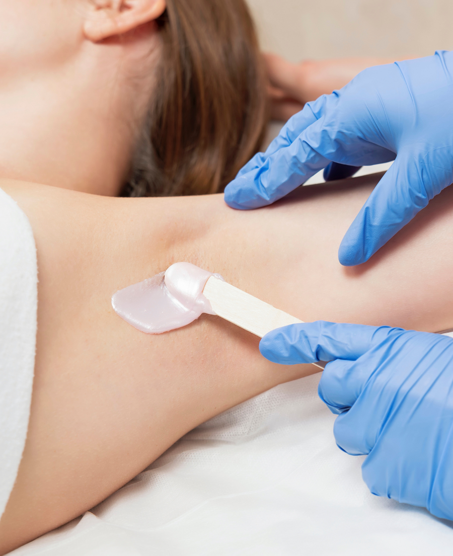 Professional esthetician removing underarm hair during a waxing service