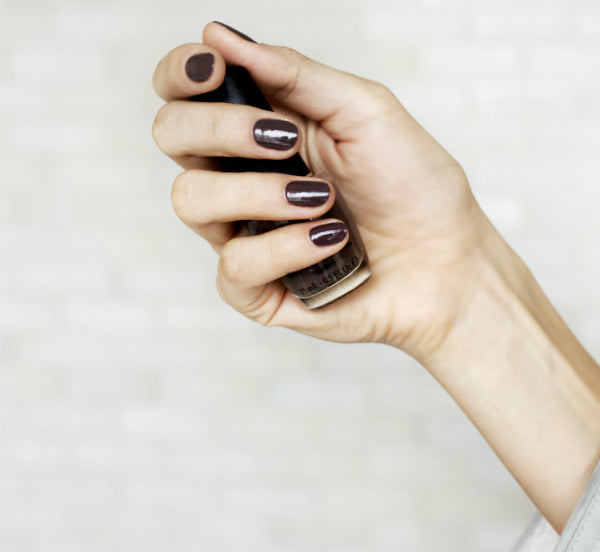 Woman's hand holding nail polish bottle. Nails painted dark color.